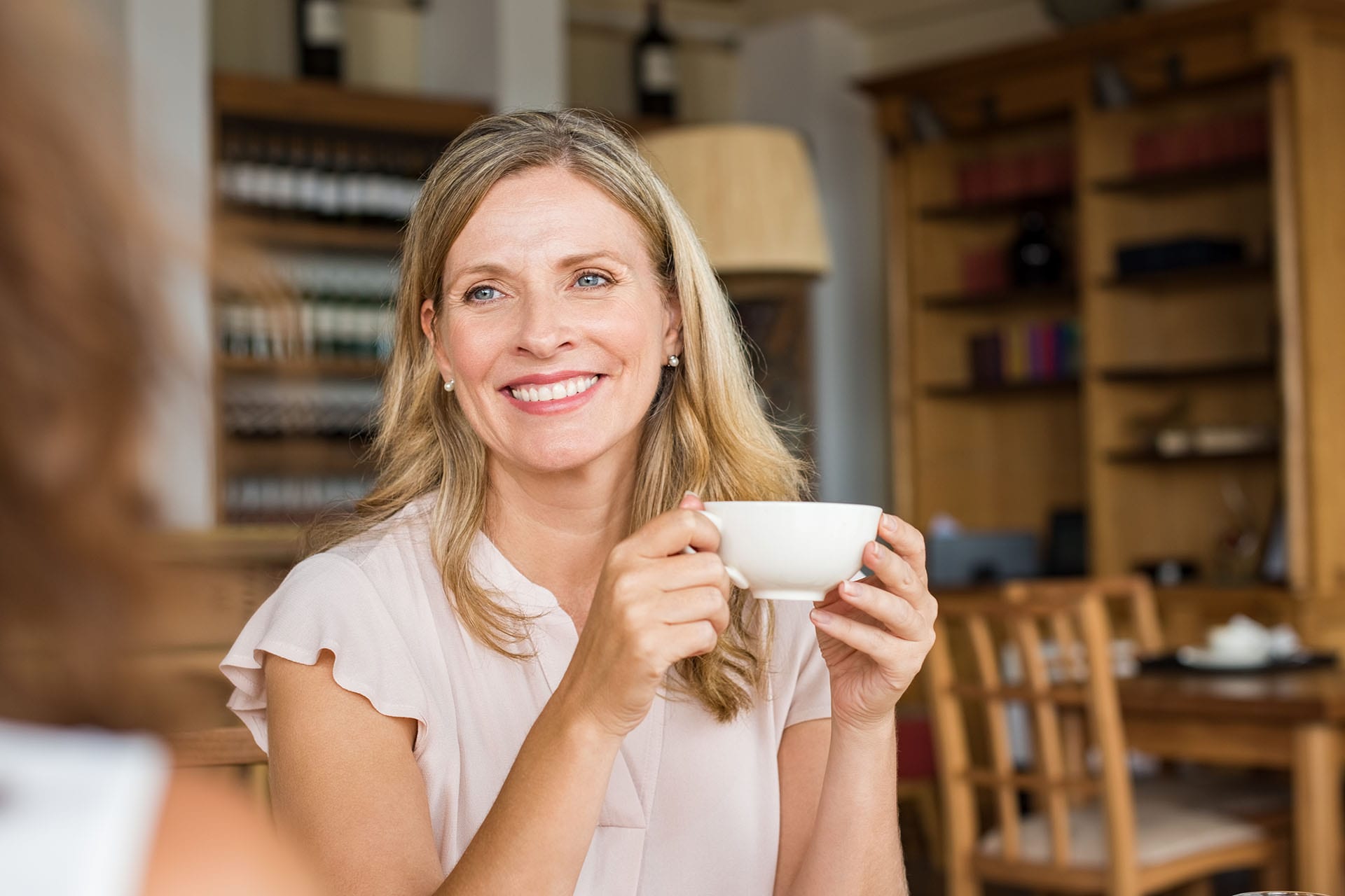 Mature woman holding coffee cup and talking with her friend.